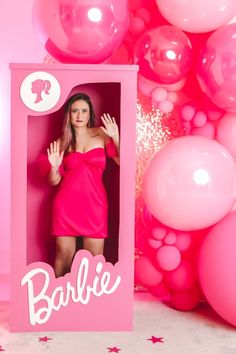 a woman in a pink dress is standing behind a photo frame with balloons around her