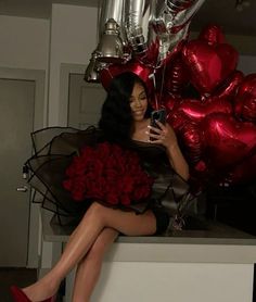 a woman sitting on top of a counter next to red balloons and holding a cell phone