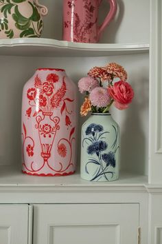 two vases with flowers are sitting on a shelf