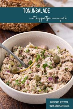 a white bowl filled with tuna salad on top of a wooden table next to a baguette