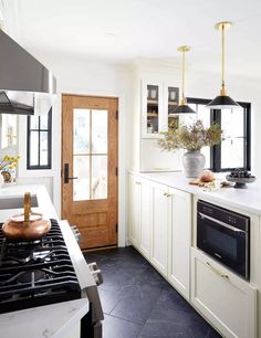 a kitchen with white cabinets and black flooring, an oven, stove top and door