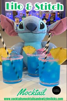 a stuffed animal sitting next to two glasses filled with blue liquid and pineapple slices