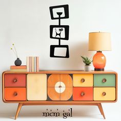 an orange and yellow dresser with a clock on it's sideboard next to a lamp