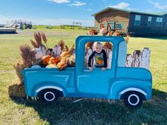 a little boy sitting in the back of a blue truck filled with hay and pumpkins