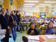 a group of children sitting at desks in a classroom with adults standing around them