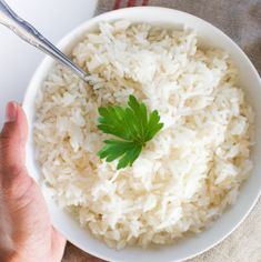 a white bowl filled with rice and garnished with a green leaf on top