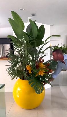 a man is standing in front of a large yellow vase with flowers and greenery