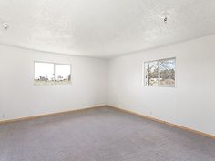 an empty room with two windows and no carpeting on the floor in front of it