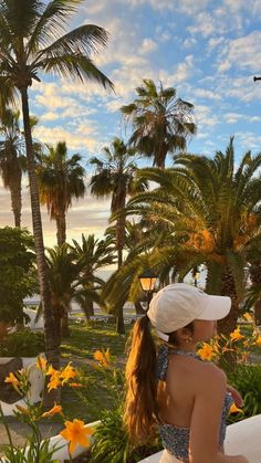 a woman sitting on a ledge looking out at the ocean and palm trees in front of her