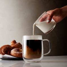 a person pouring milk into a cup next to pastries