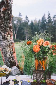 carrots and other vegetables are arranged in a vase on a table outside near a tree