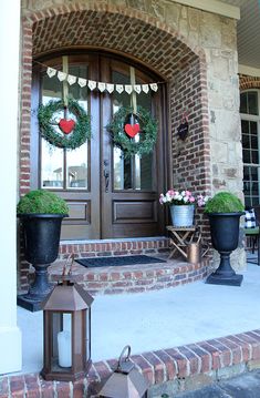 the front door is decorated for valentine's day with wreaths and potted plants