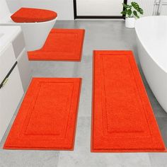 three orange rugs are on the floor in front of a bathtub and sink