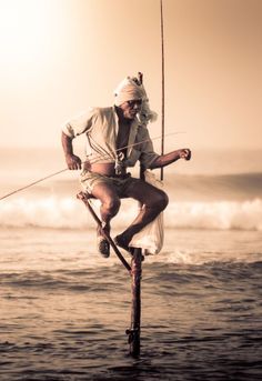 a man is standing on a pole in the ocean holding onto a fishing rod with one hand