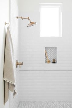 a white tiled bathroom with gold fixtures and towels hanging on the shower head, along with two brass faucets