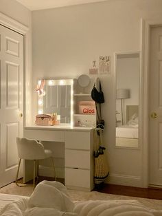 a bedroom with white furniture and lights on the mirror above the vanity, along with two chairs