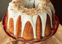 a bundt cake with white icing and nuts on top sits in a glass dish