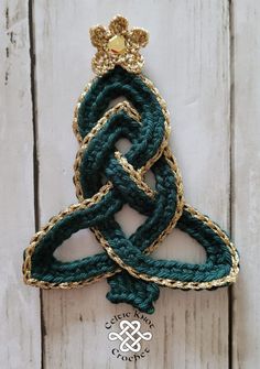 a green and gold brooch sitting on top of a white wooden table next to a piece of wood