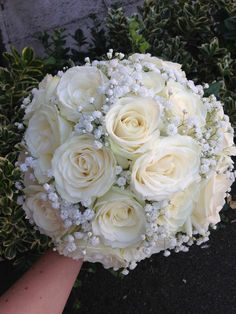 a bouquet of white roses and baby's breath is held by someones hand