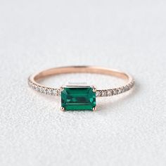 an emerald and diamond ring on a white surface