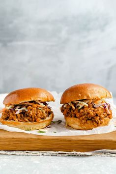 two sloppy joe sandwiches sitting on top of a cutting board