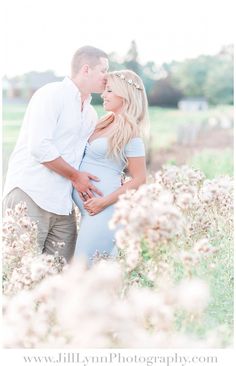 a pregnant couple standing in a field with flowers