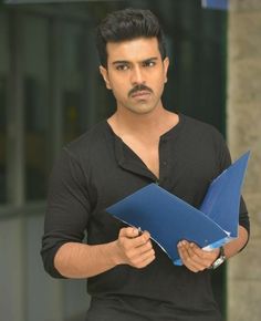 a man holding a blue folder in his right hand and looking at the camera with a serious look on his face