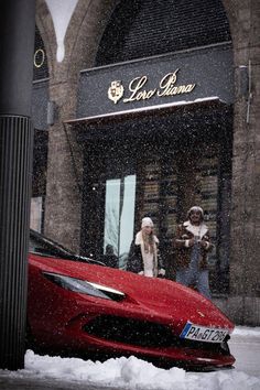 a red sports car parked in front of a building on a snowy day with people walking by