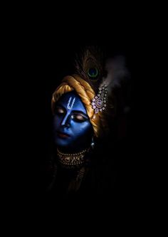 a woman with blue face paint and peacock feathers on her head, in the dark