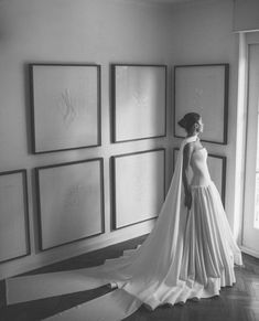 a woman in a wedding dress standing next to some framed art on the wall and looking at it