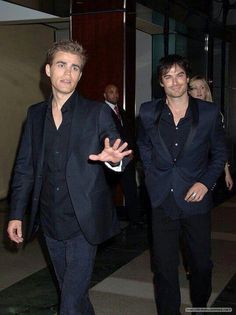 two young men dressed in black walking down a hall way with one holding his hand out