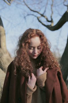 a woman with long red hair standing in front of a tree