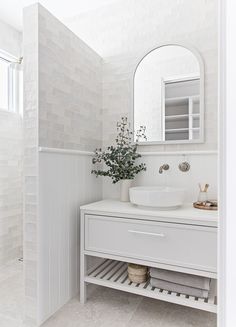 a white bathroom with a sink and mirror on the wall next to a shelf that has a potted plant in it