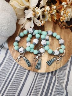 several bracelets with tassels and charms on a wooden board next to flowers