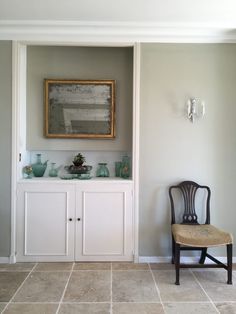 a chair sitting in front of a white cabinet with glass vases on top of it