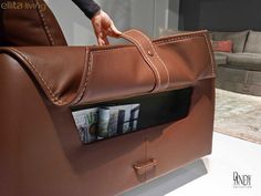 a person holding a brown leather bag with magazines in it's pocket on display