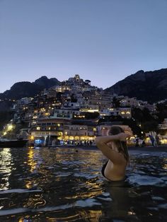 a woman is sitting in the water at night with buildings on top of her head