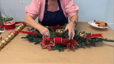 a woman is decorating a christmas wreath with red and gold ribbons on a table