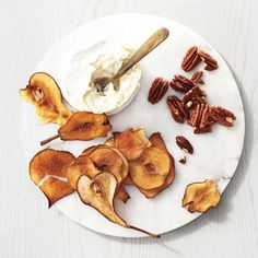 a white plate topped with sliced apples and whipped cream next to pecans on a table