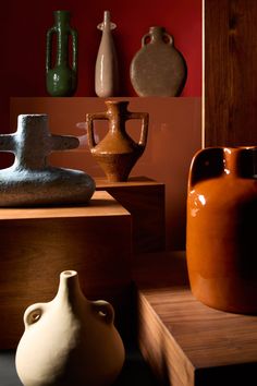 several vases are sitting on display in a room with red walls and wooden shelves