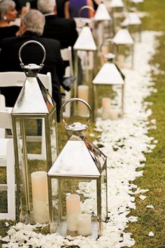 rows of white lanterns lined up on the grass with flowers and petals all over them