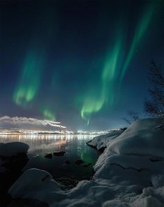 the northern lights shine brightly over water and snow