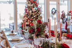 a table set for christmas dinner in front of a tree with red and green decorations