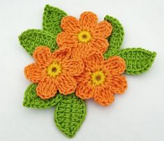 crocheted orange and green flowers with leaves on white table top, ready to be made into brooch or pin