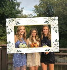 three young women standing next to each other in front of a photo frame with flowers on it