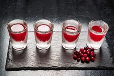 four shot glasses filled with red liquid and cranberries