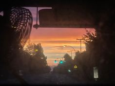 the sun is setting over an intersection with trees and street lights in the foreground