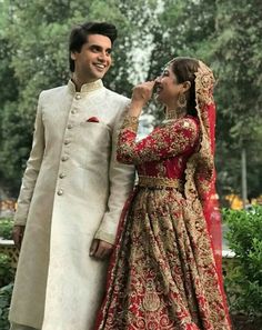 two people standing next to each other in wedding outfits, one wearing a red and gold outfit