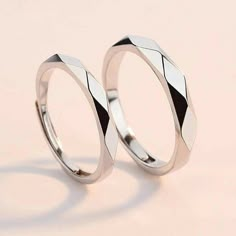 two wedding rings sitting next to each other on a pink surface with one ring in the middle