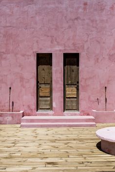 a pink building with two windows and wooden steps